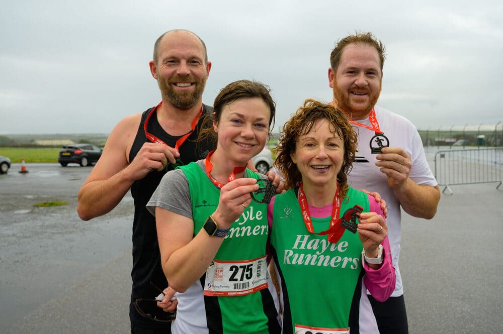 Group Of Four Runners Smiling And Holding Their Medals
