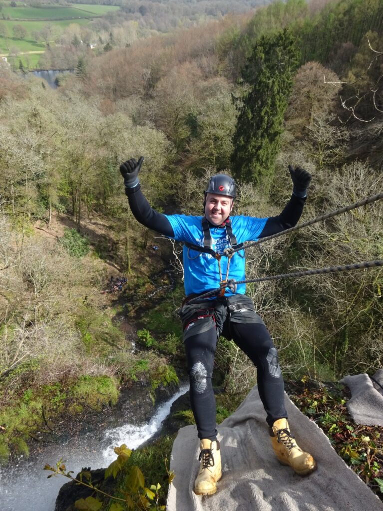 Man abseiling off a tall cliff with thumbs up and smile