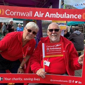 Two Cornwall Air Ambulance volunteers at event posing behind red frame