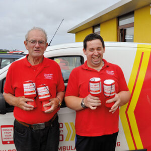 Two Cornwall Air Ambulance volunteer money pot cleaners stood infant of charity car holding money pots.