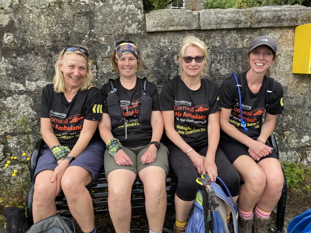 Lynnette and her three female friends sat on a bench in a row in their walking gear, taking a break on the Saints Way.