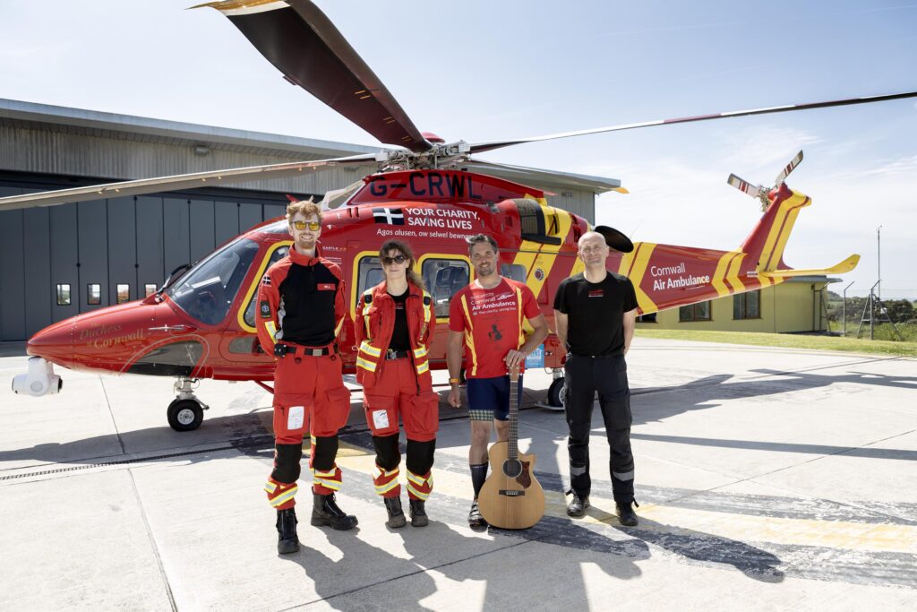 Tom standing in a line with three Cornwall Air Ambulance team members on the landing pad with the red helicopter behind them.
