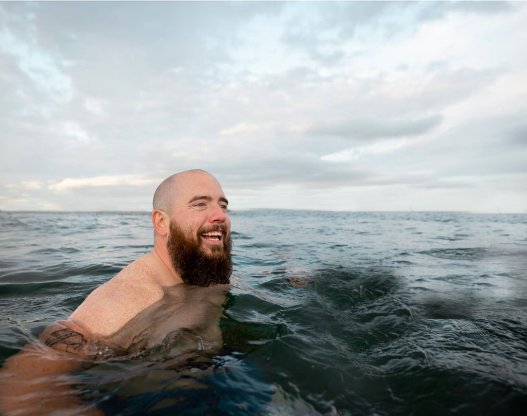 Man in ocean smiling, embracing the cold water swim