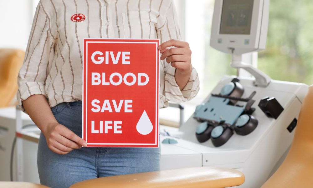 A female holding a red sign that says 'give blood, save life.'